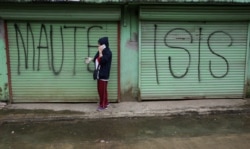FILE - A man is seen using a mobile phone while passing a shuttered store front with "MAUTE-ISIS" graffiti, in Marawi city, southern Philippines, Oct. 20, 2017. Maute, an Islamic State affiliate, was among groups the U.S. added to its terror list Tuesday.