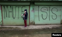 FILE - A man is seen using a mobile phone while passing a shuttered store front with "MAUTE-ISIS" graffiti, in Marawi city, southern Philippines, Oct. 20, 2017. Maute, an Islamic State affiliate, was among groups the U.S. added to its terror list Tuesday.