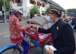 Berbusana adat Jawa dan bermasker, relawan membagikan masker dan hand sanitizer gratis untuk tukang becak, juru parkir, pedagang pasar dan kuli gendong di Paaar Gedhe Solo, 21 Maret 2020. (Foto: VOA/Yudha Satriawan)