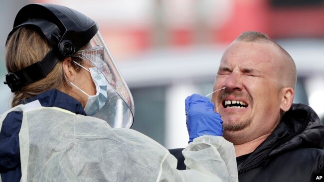 In this April 17, 2020, file photo, a man reacts as a medical staffer tests shoppers who volunteered at a pop-up community COVID-19 testing station at a supermarket carpark in Christchurch, New Zealand. (AP Photo/Mark Baker,File)