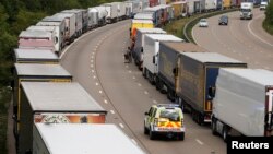 A police vehicle drives past trucks backed up on the M20 motorway which leads from London to the Channel Tunnel terminal at Ashford and the Ferry Terminal at Dover, June 23, 2015.