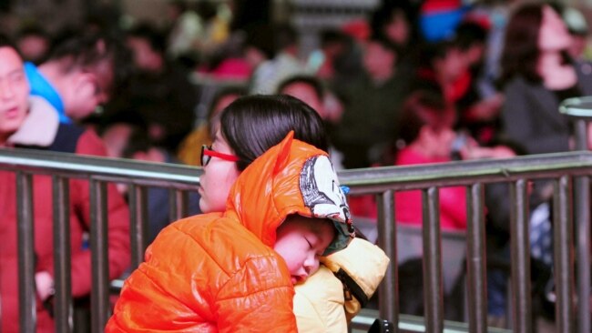 一名中国妇女带着小孩在春运时期的火车站等待上车 (资料图片)