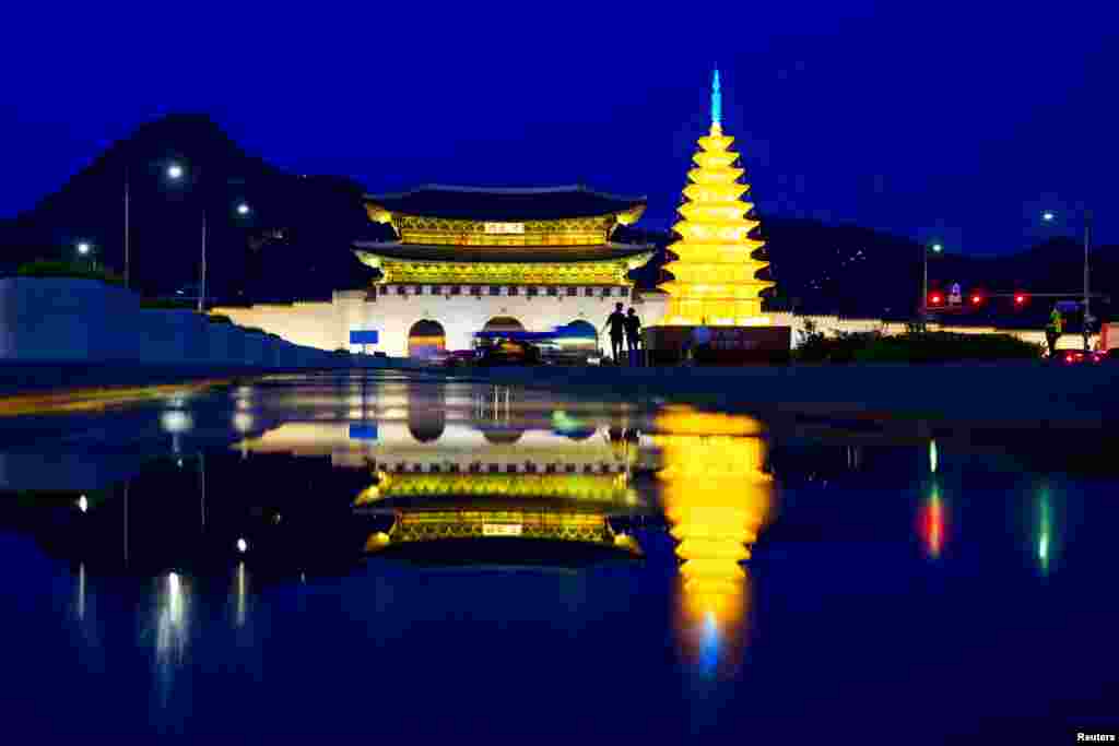 A couple walk past an illuminated pagoda as the gate of the Gyeongbokgung Palace is reflected in water in Seoul, South Korea.