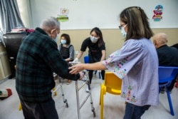 Pemilik salon Cass Ng membantu seorang lansia sebelum memberinya pelayanan pedikur di pusat komunitas lansia di Hong Kong sebagai bagian dari inisiatif amal, 8 November 2021. (Foto: AFP/Isaac Lawrence)