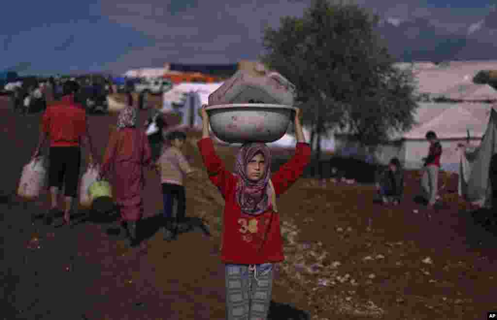 在靠近土耳其边界的叙利亚村庄阿特玛的一处难民营，一名叙利亚女孩头顶塑料容器走去打水。她和家人逃难到这里。（2012年11月10日）