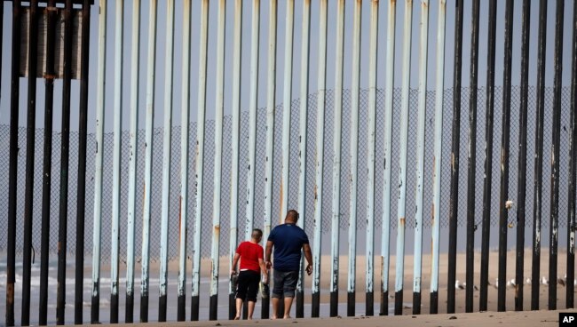 FILE - Two people walk towards metal bars marking the United States border where it meets the Pacific Ocean, in Tijuana, Mexico, March 2, 2016.