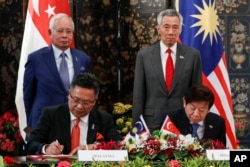 FILE - Malaysia's then-Prime Minister Najib Razak, and Singapore's PM Lee Hsien Loong witness the signing of an agreement on the Johor Bahru-Singapore Rapid Transit System Link at the Istana or presidential palace in Singapore, Jan. 16, 2018.