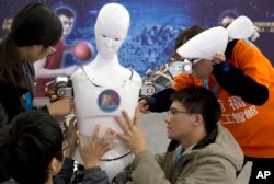 FILE - Chinese students work on the Ares, a humanoid bipedal robot, displayed during the World Robot Conference in Beijing, Oct. 21, 2016.