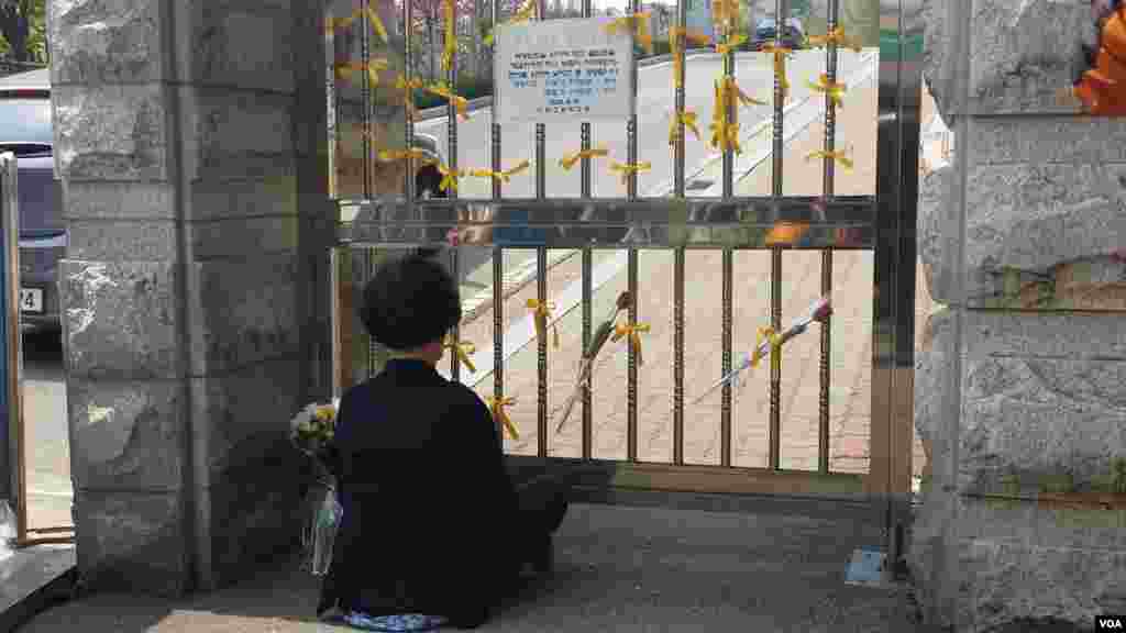 한국 세월호 침몰사고 희생자들이 다니던 안산시 단원고등학교 후문이 폐쇄되어 있는 가운데, 희생자를 애도하는 여성이 교문 앞에 앉아있다.