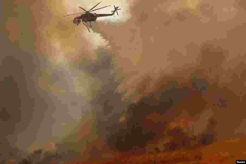 A helicopter drops water on a wind driven wildfire in Orange, California, Oct. 9, 2017.