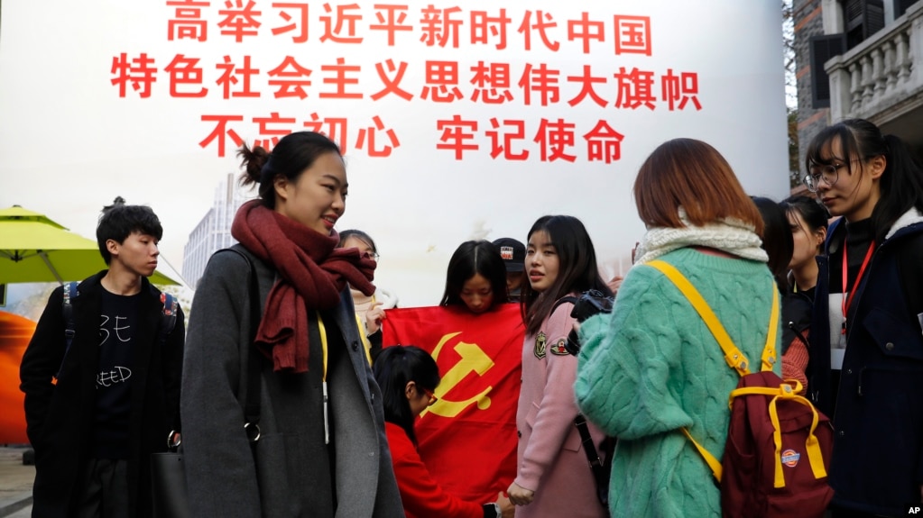 资料照:上海大学生在一幅宣传习近平的大标语前照相后将一面中共党旗收起来。(2017年11月19日)
