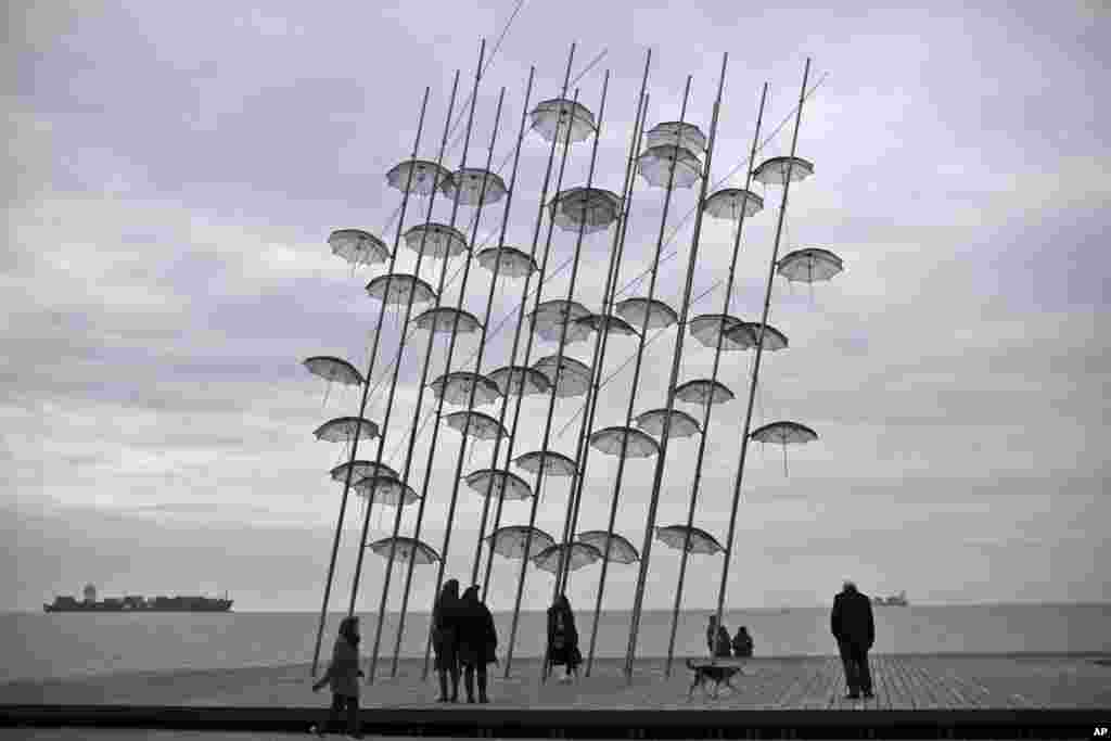 A woman poses for a picture taken by her friends by the &quot;Umbrellas&quot; sculpture, by George Zongolopoulos, on the seafront of the northern Greek city of Thessaloniki.