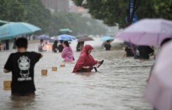 Warga mengarungi jalan yang banjir di tengah hujan deras di Zhengzhou, Provinsi Henan, China, 20 Juli 2021. (Foto: China Daily via REUTERS)