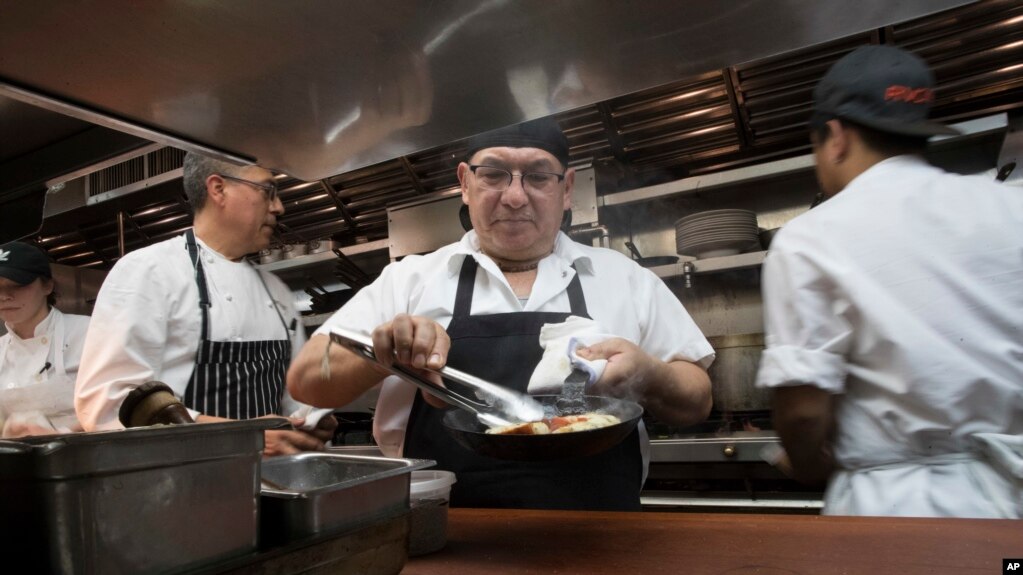 In this Nov. 27, 2018 photo, Chef Jacinto Guadarrama, left, prepares dishes with the help of the kitchen staff at Gotham Bar and Grill in New York. For businesses in many states, including New York, the minimum wage is now $15 an hour.