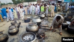 FILE - A Pakistani non-governmental humanitarian organization volunteer (front) adjusts a cooking fire as locals line up to receive meals in Nowshera, in Pakistan's northwest Khyber-Pakhtunkhwa Province, Sept. 10, 2010. Foreign-funded local organizations in northwestern Pakistan provide humanitarian and emergency assistance, including health, education, and food distribution, to more than two million people who have been displaced by ongoing Pakistani military operations against militant groups.