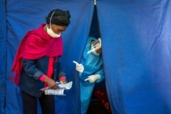 FILE - Heath officials check the listings of people who are to be tested for COVID-19 as well as HIV and Tuberculosis, in downtown Johannesburg, April 30, 2020.