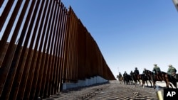 FILE - Mounted Border Patrol agents ride along a newly fortified border wall structure in Calexico, California, Oct. 26, 2018. The U.S. program to send asylum-seekers back to Mexico to wait out their U.S. court proceedings has been expanded to the Calexico port.