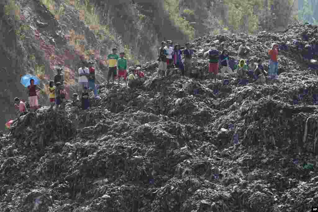 Workers and residents stand on a mountain of garbage at a landfill during a rescue operation in San Isidro, Rizal province, east of Manila, Philippines. Police said four workers were reportedly missing after a garbage landfill slid along a mountainside.
