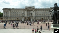 FILE - People are seen in front of Britain's Queen Elizabeth II's official London residence, Buckingham Palace, in London.