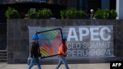 Employees walk in front of a banner at the government complex where the Asia-Pacific Economic Cooperation (APEC) Summit will take place in Lima on November 13, 2024.