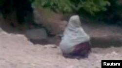 A woman accused of adultery squats in front of a crowd before her public execution by a man who Afghan officials say is a member of the Taliban, in a village outside Kabul in this still image taken from undated footage released July 7, 2012. 