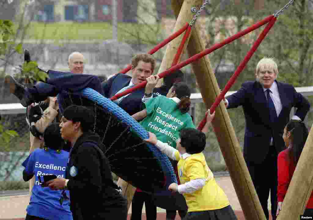 Britain&#39;s Prince Harry plays on a swing with children as Mayor of London Boris Johnson (R) looks on during a viewing of Queen Elizabeth Olympic Park ahead of its opening on April 5, 2014, at Stratford in east London.