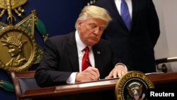 FILE - President Donald Trump signs an executive order to impose tighter vetting of travelers entering the United States, at the Pentagon in Washington, Jan. 27, 2017. 
