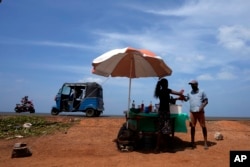 FILE - A man buys a cool drink from a roadside vendor on a sunny day in Mahawewa, a village north of Colombo, Sri Lanka, Feb. 29, 2024. (AP Photo/Eranga Jayawardena, File)