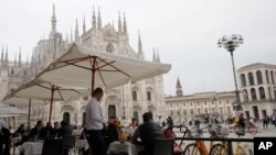 A waiter talks to clients sitting at a restaurant backdropped by Milan's gothic cathedral, April 26, 2021, as Italy is gradual reopening after six months of rotating virus closures.