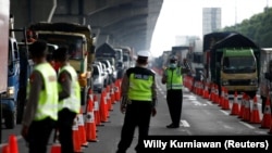 Seorang petugas polisi mengenakan masker bergerak ke ketika menjaga sebuah pos pemeriksaan jalan raya menyusul larangan pemerintah terhadap eksodus massal mudik tradisional untuk mencegah penyebaran wabah virus corona, di Bekasi, 24 April 2020. (Foto: Reuters/Willy Kurniawan)