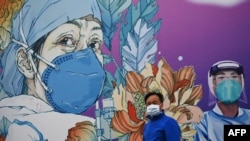 FILE - A man wearing a face mask walks in front of a mural at the Leishenshan Hospital that had offered beds for coronavirus patients in Wuhan, in China’s central Hubei province on April 11, 2020.