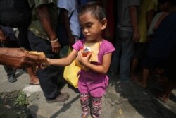 FILE - A poor Filipino girl holds bread and drinks she received during a feeding program by Dominican nuns in Manila, Philippines on Sept. 17, 2014.