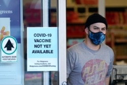 FILE - A customer wearing a mask walks out of a Walgreen's pharmacy store and past a sign advising that COVID-19 vaccines are not available there yet during the coronavirus outbreak, December 2, 2020.