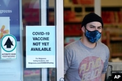 FILE - A customer wearing a mask walks out of a Walgreen's pharmacy store and past a sign advising that COVID-19 vaccines are not available there yet during the coronavirus outbreak, December 2, 2020.