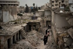 FILE - Women walk in a neighborhood heavily damaged by airstrikes, in Idlib, Syria, March 12, 2020.