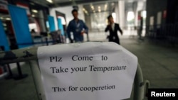 A sign requesting people to come have their temperature taken is seen at the entrance to the Canton Fair in Guangzhou, Guangdong province, Oct. 26, 2014.