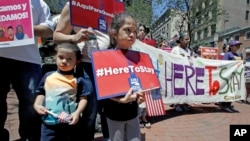 FILE - Nicole Castillo, 7, of East Boston, holds a sign while standing with her brother Diego, 4, and mother Elsa, who is originally from El Salvador, during a "Here to Stay" rally at the Irish Famine Memorial in Boston, July 6, 2017.