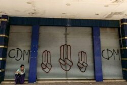 FILE - A man sits in front of shutters decorated with graffiti in support of the civil disobedience movement (CDM) and the three-finger salute made by protesters demonstrating against the military coup in Yangon, April 7, 2021.