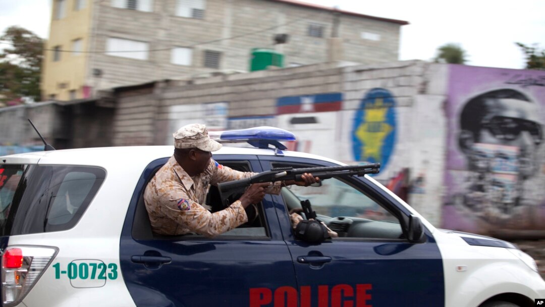 A Haitian national police officer fires birdshot at demonstrators during a street protest after it was announced that the Jan. 24 runoff election had been postponed, in Port-au-Prince, Jan. 22, 2016.