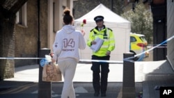 ARCHIVO - Una mujer lleva una flor a la escena del crimen en Link Street, Hackney, al este de Londres, el jueves 5 de abril de 2018.