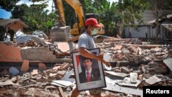 Seorang pria menenteng gambar Presiden Joko Widodo dari sekolah yang rusak akibat gempa di Gunungsari, Lombok, 12 Agustus 2018.
