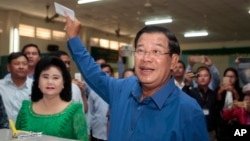 Cambodian Prime Minister Hun Sen of the Cambodian People's Party shows off his ballot paper next to his wife, Bun Rany, foreground left, before voting in local elections at Takhmau polling station in Kandal province, southeast of Phnom Penh, Cambodia, Sunday, June 4, 2017. (AP Photo/Heng Sinith)