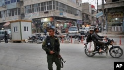 FILE - A member of the Kurdish internal security forces patrols a commercial street in Manbij, north Syria, March 28, 2018. 