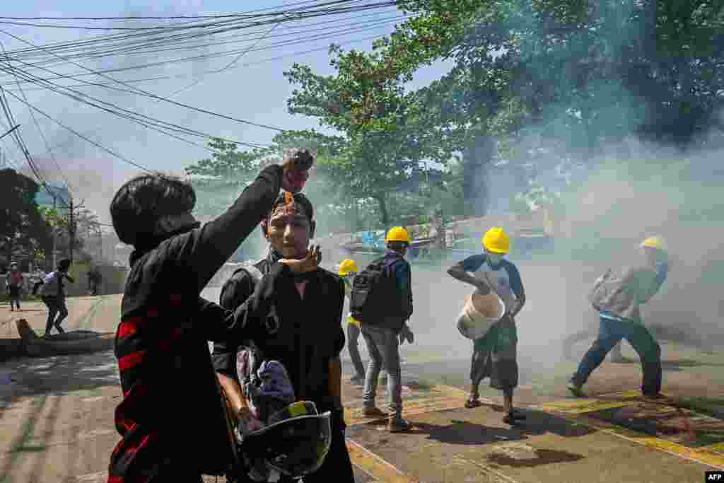 미얀마 양곤의 군부 쿠데타 반대 시위 참가자들이 경찰의 최루 가수를 뿌리기 위해 얼굴에 음료수를 뿌리고 있다.