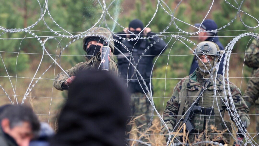 Polish border guards stand near the barbed wire as migrants from the Middle East and elsewhere gather at the Belarus-Poland border near Grodno, Belarus, Monday, Nov. 8, 2021. Poland increased security at its border with Belarus, on the European Union's eastern border, after a lar
