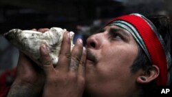 In this Friday, May 3, 2019 photo, a resident blows on a conch shell to honor Tonantzin, the Aztec mother earth goddess during the Day of the Cross celebrations on the flanks of the Iztaccíhuatl volcano or The Sleeping Woman. (AP Photo/Marco Ugarte)