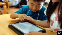 FILE - Children work on a digital program at Coby Preschool in Yoshikawa, suburban Tokyo, on an assignment, which was to draw on a triangle on an iPad, July 12, 2018.