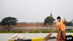 A cleaner wearing a face mask sweeps a road near the ramparts of the former royal palace