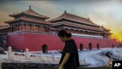 Una mujer mira su teléfono mientras camina delante de un cartel con la imagen de la Ciudad Prohibida en una estación de metro de Beijing, China, el martes 16 de julio de 2024.