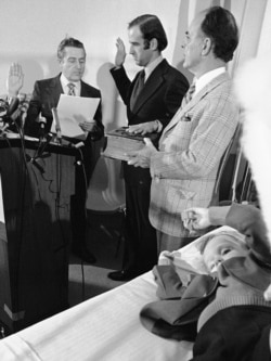 FILE - Four-year-old Beau Biden, foreground, plays near his father, Joe Biden, center, as he is sworn in as the U.S. senator from Delaware, by Senate Secretary Frank Valeo, left, in ceremonies in a Wilmington hospital, Jan. 5, 1973.